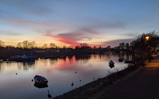 A sunset image over a river with small boats and geese wading.